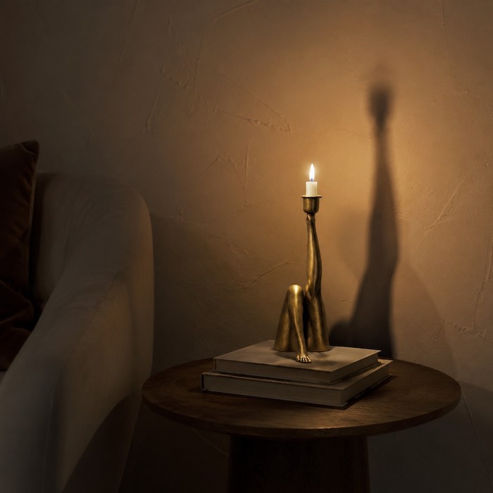 Curved sculptural candle holder casting dynamic shadows on a wall in a moody room.
