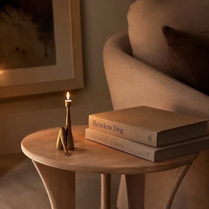 A slender, artistic sculptural candle holder styled on a compact wooden side table.