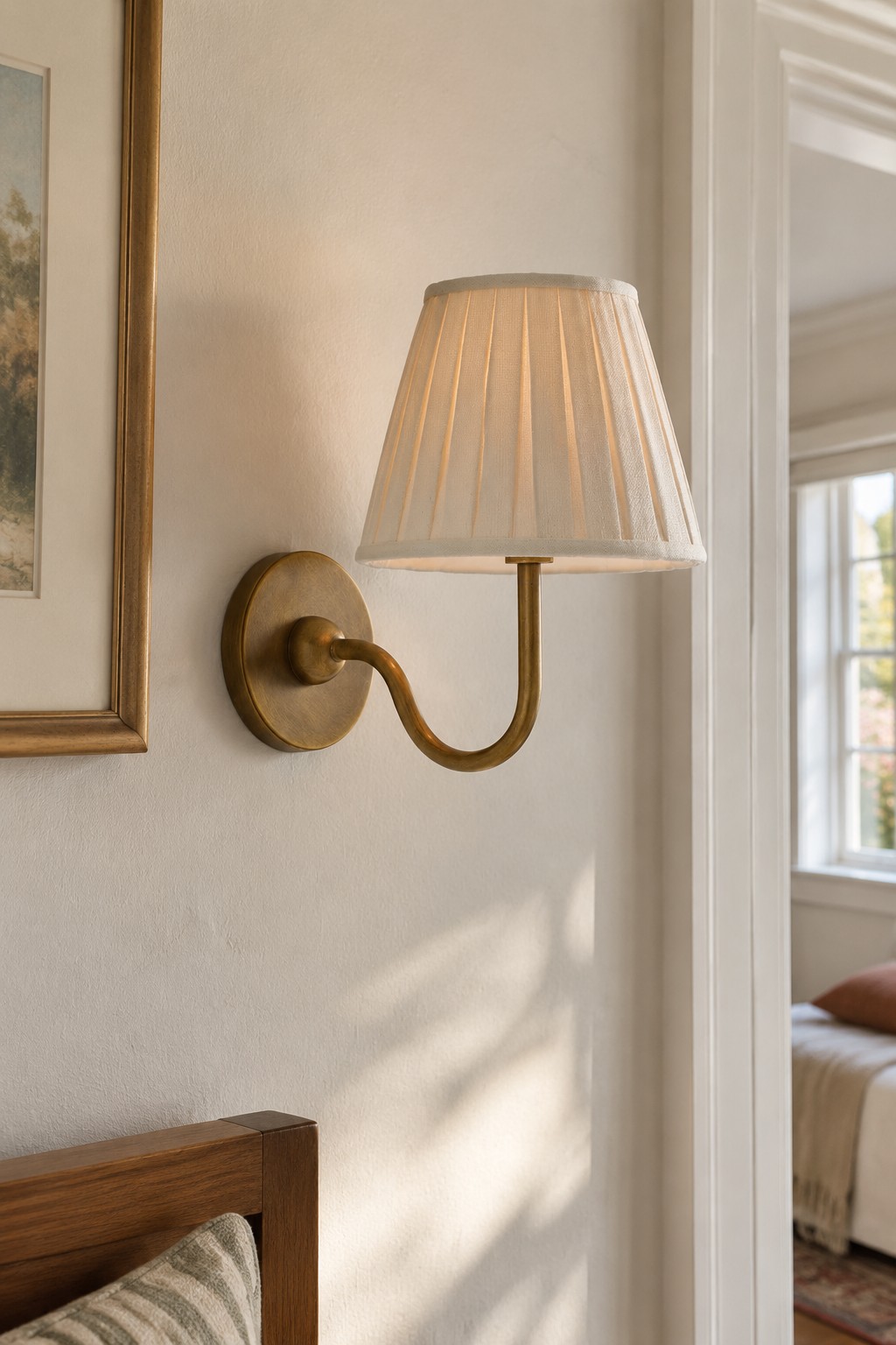 A brass wall light with a cream pleated shade