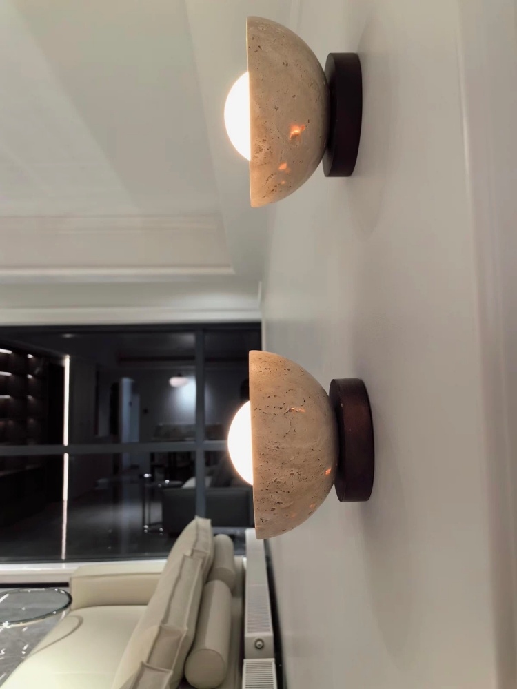 Travertine wall lights glowing beside a mirror