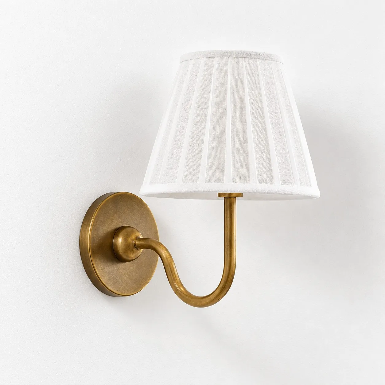 White pleated linen shade on a tumbled brass wall lamp