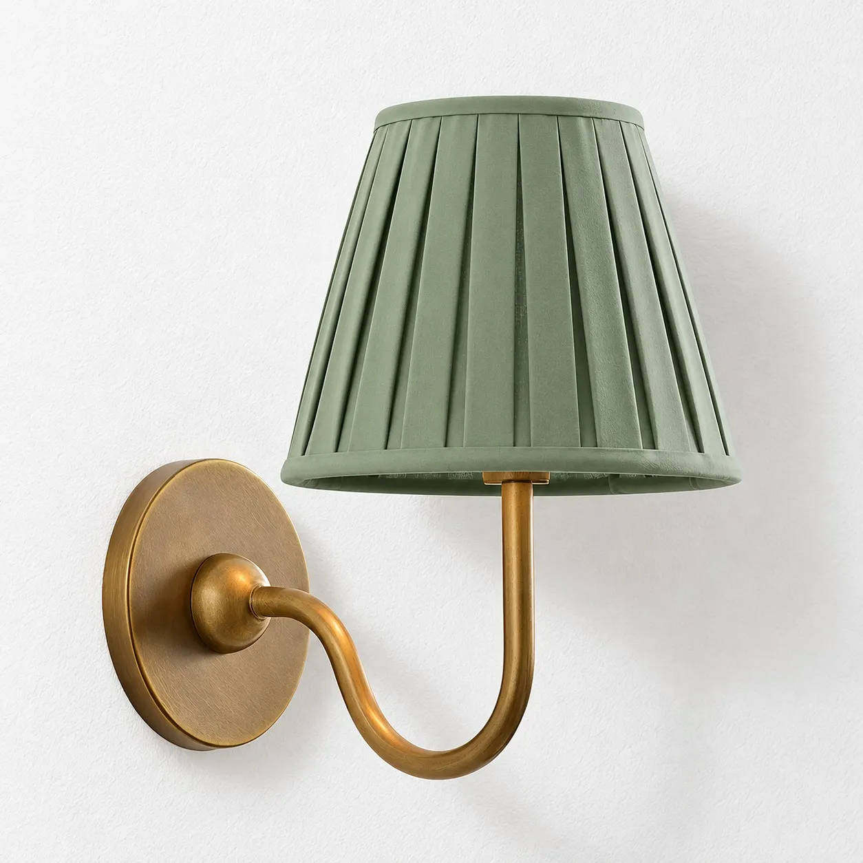 Sage green pleated linen shade on a tumbled brass wall lamp