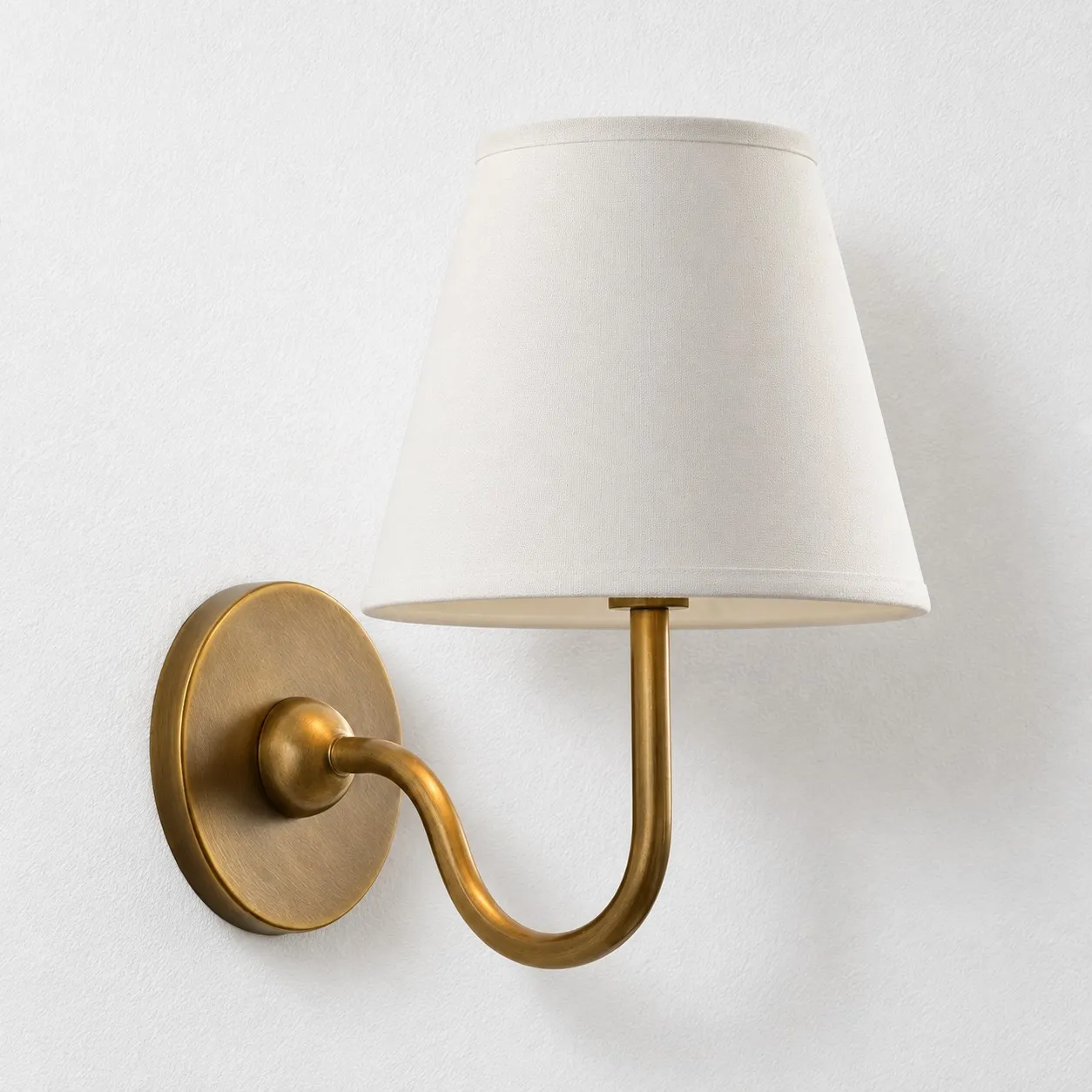 White plain linen shade on a tumbled brass wall lamp