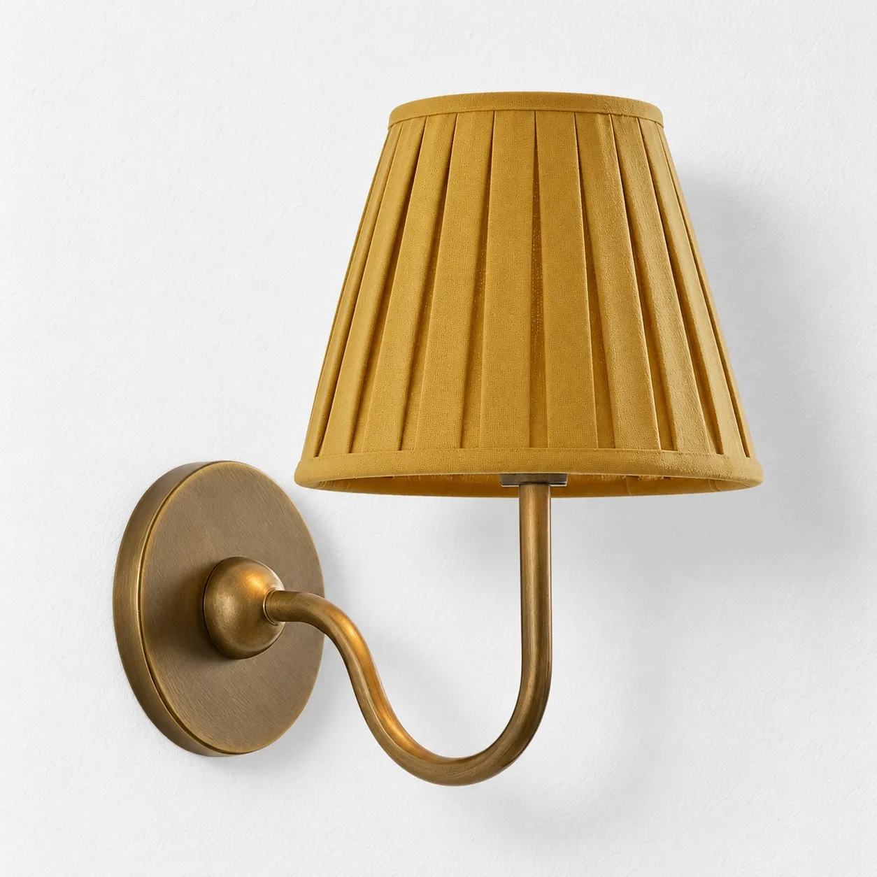 Mustard yellow pleated linen shade on a tumbled brass wall lamp
