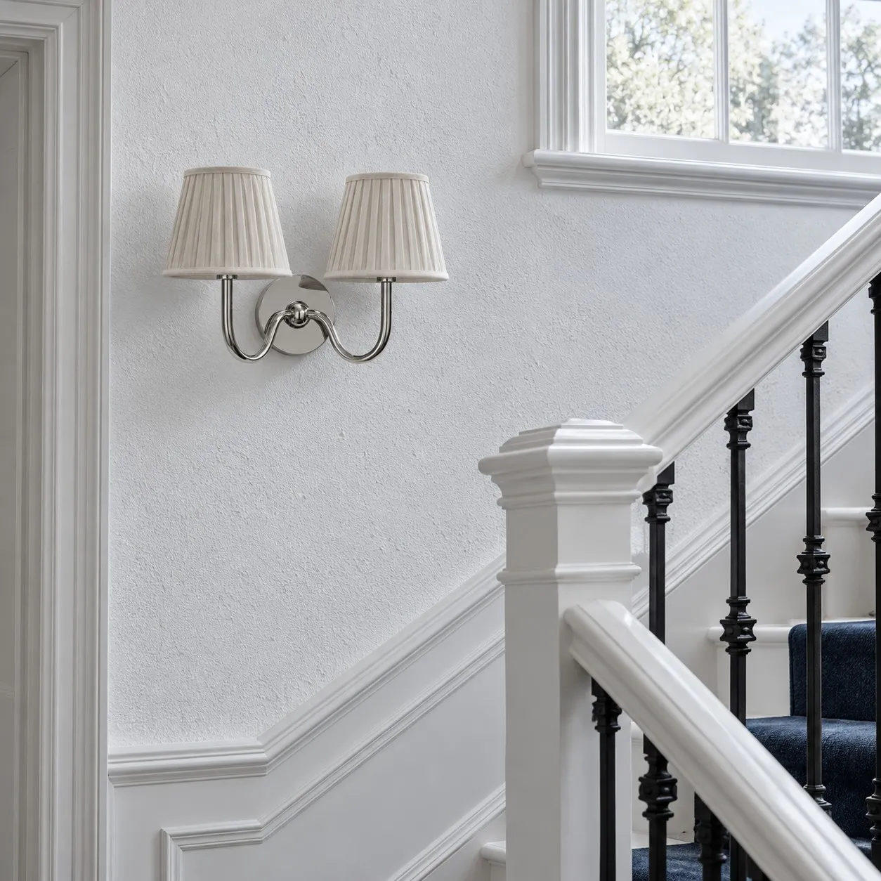 Chrome two-light wall lamp with white pleated shades beside a stair